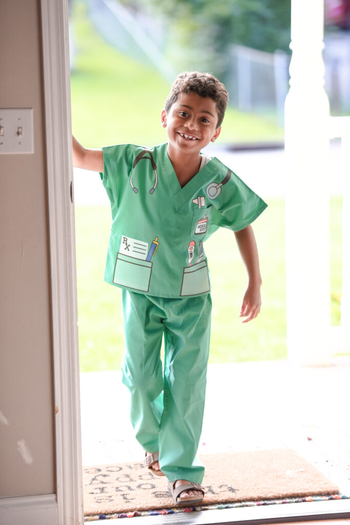 boy wearing scrubs with vinyl decals to show prescription pad in pocket, thermometer in other pocket, reflex hammer in 3rd pocket, and stethoscope over shoulders