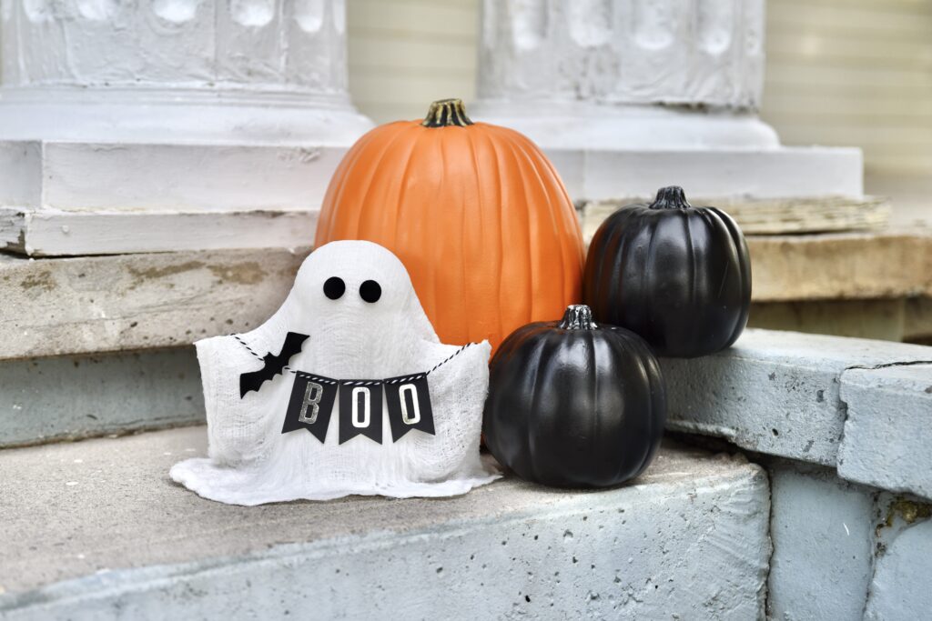 stiffened cheesecloth made into a ghost holding a banner that says Boo and has a black bat on it