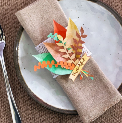 Thanksgiving napkin ring with various shapes and colors of leaves and text saying thankful