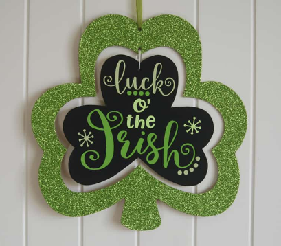 Green shamrock shaped sign with middle section that looks like black chalkboard and says luck o' the Irish