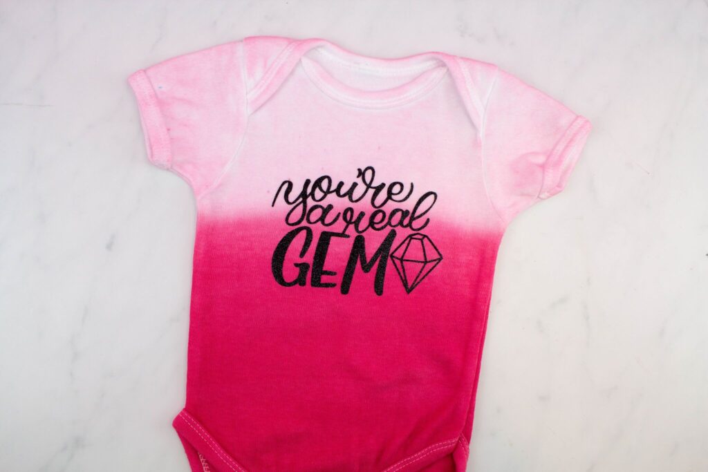 DIY dip dyed baby onesie that says "You're a real gem" on it