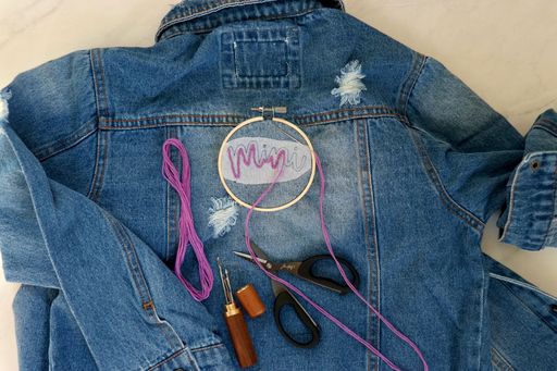 Embroidery being put on the back of a denim jacket saying Mini