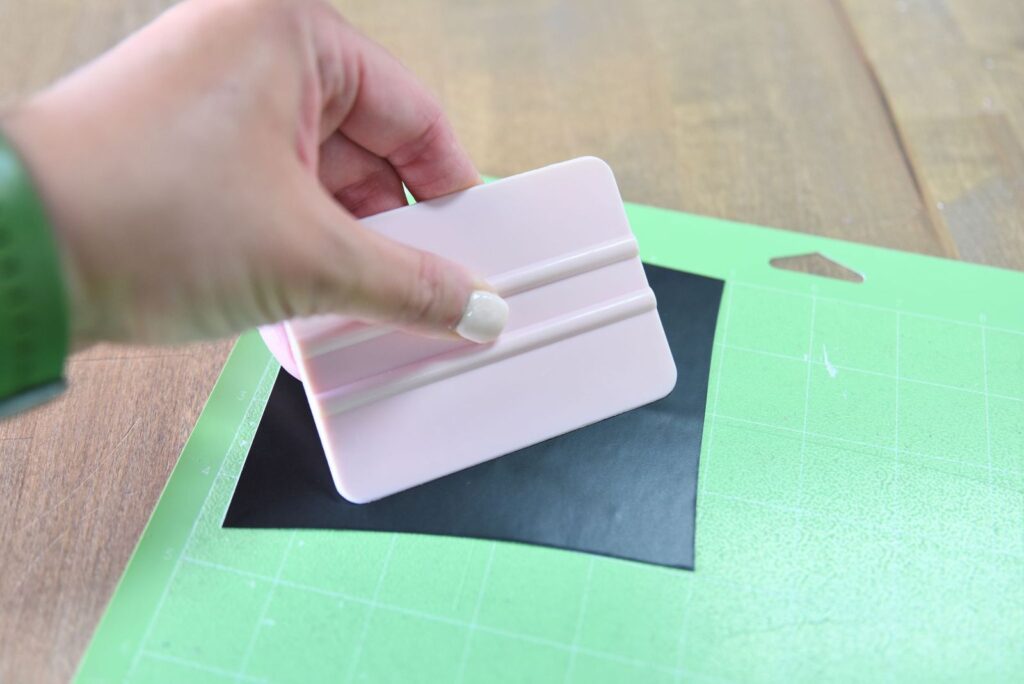 using a scraper tool to burnish vinyl onto the cutting mat