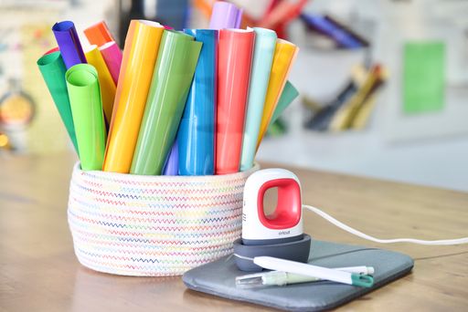 rolls of vinyl in a basket with a cricut easy press mini and weeding tools