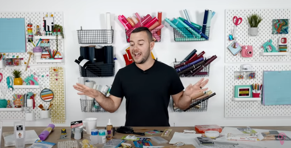 Man Standing At A Table Full Of Dollar Store Craft Supplies